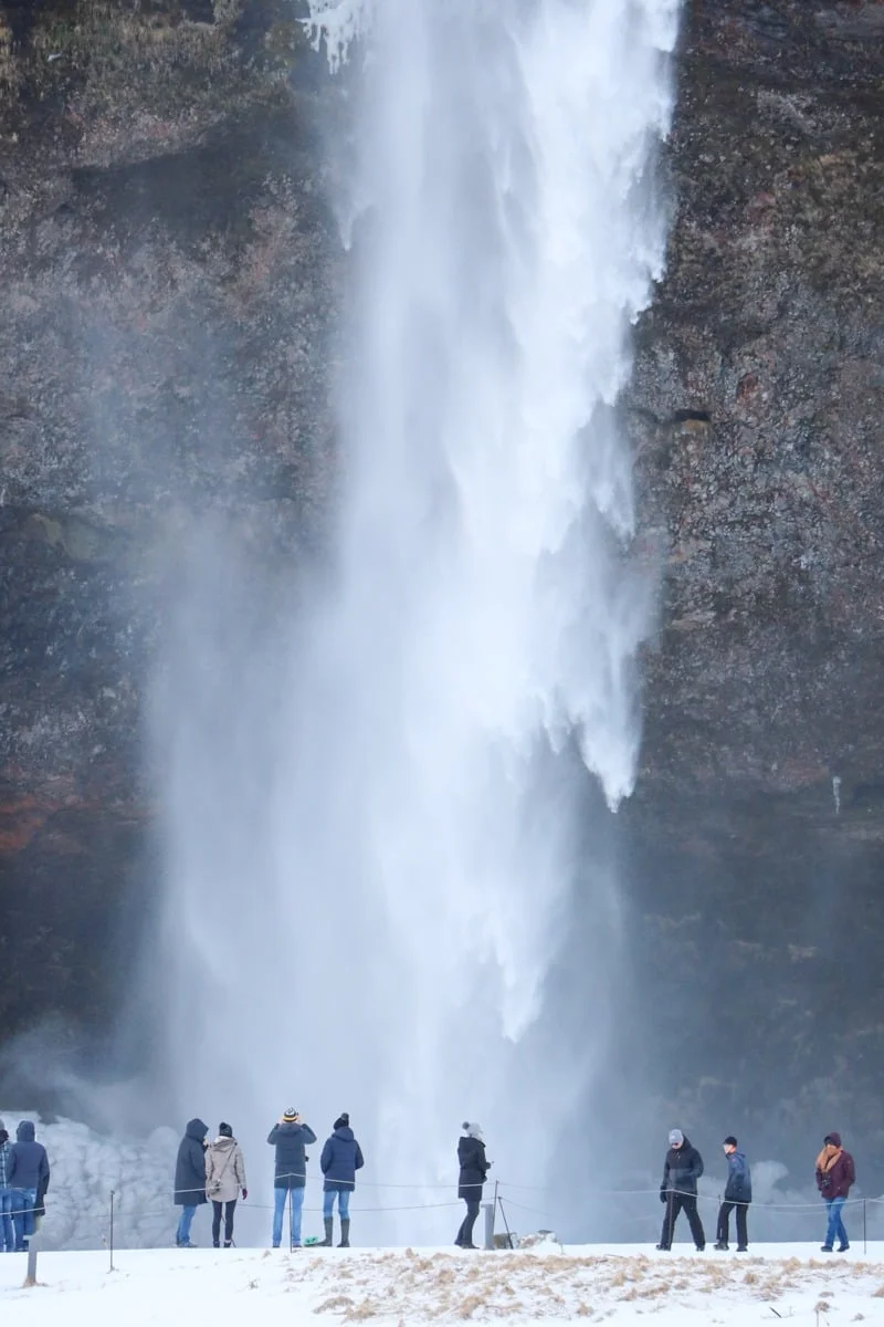 Groupe de visiteurs debout face à une grande cascade en hiver