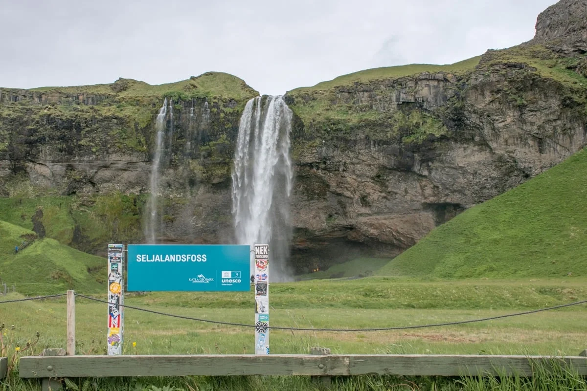 Panneau touristique devant une grande cascade tombant d'une falaise verdoyante