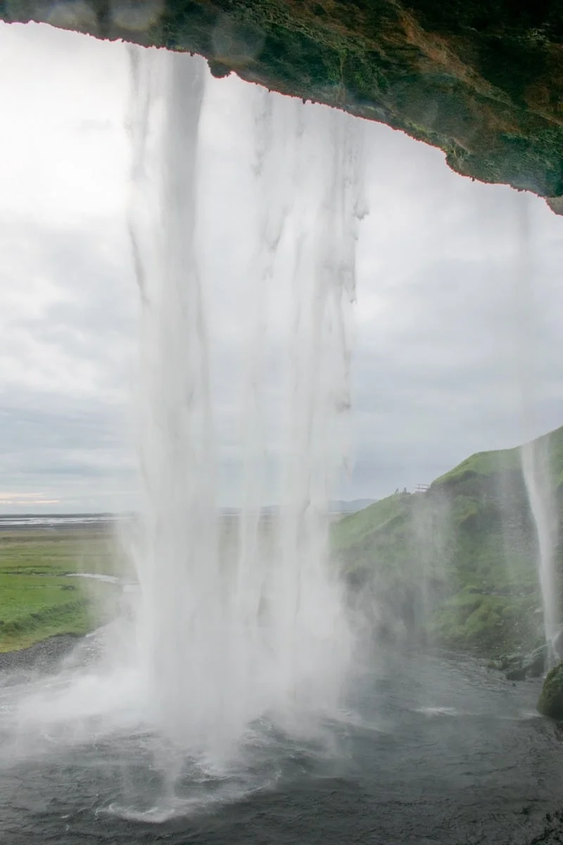 Vue depuis l'intérieur d'une cascade, brume et collines verdoyantes au loin