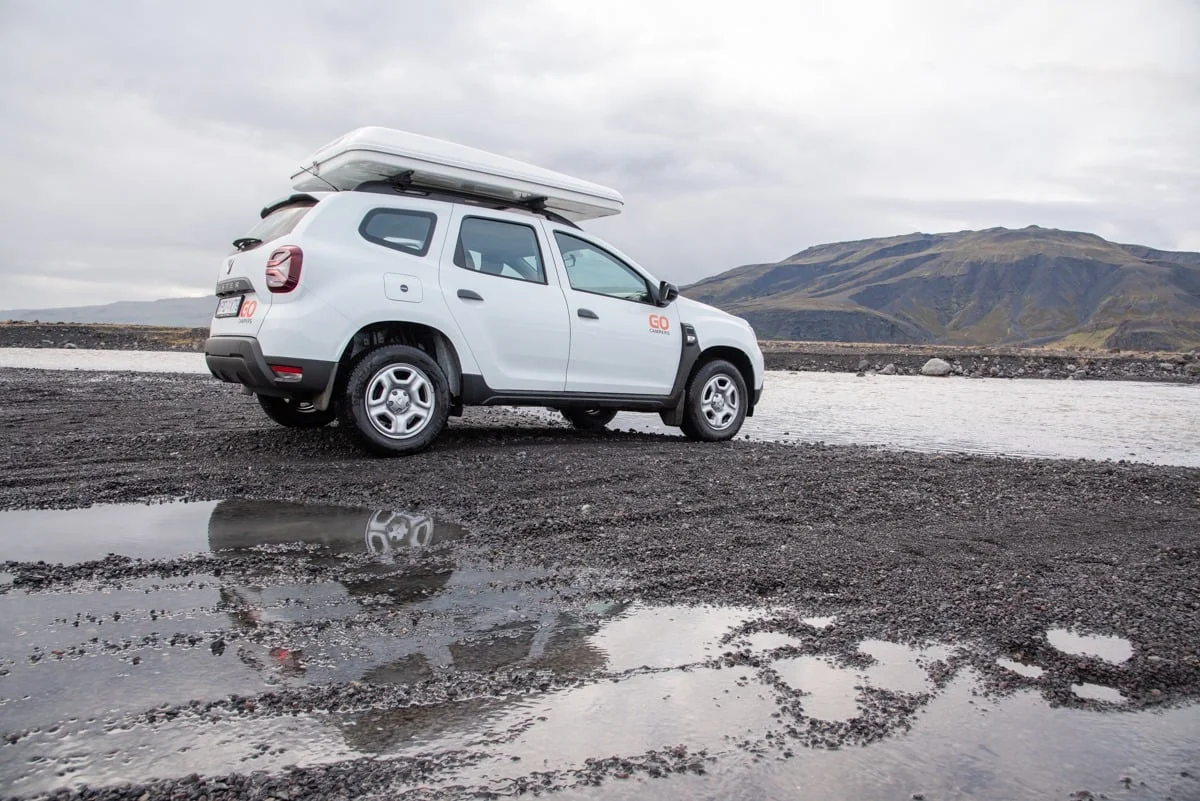SUV blanc avec tente de toit garé sur terrain volcanique humide