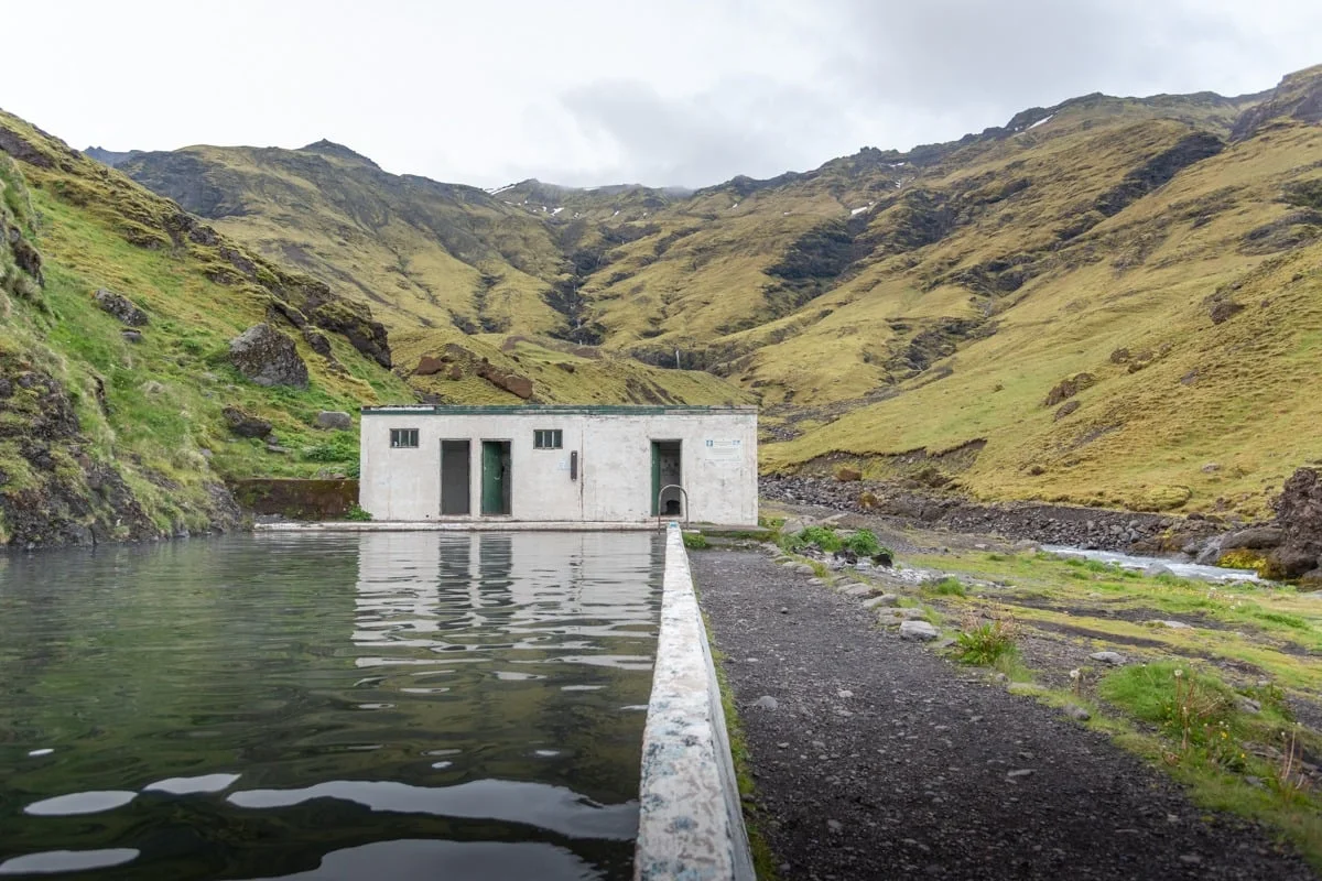 Piscine naturelle avec bâtiment blanc entouré de montagnes verdoyantes