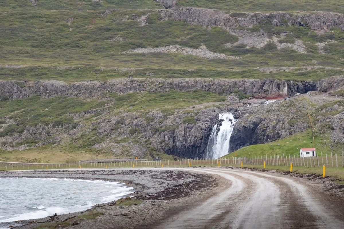 Piste de gravier longeant la mer vers une cascade sur falaise rocheuse