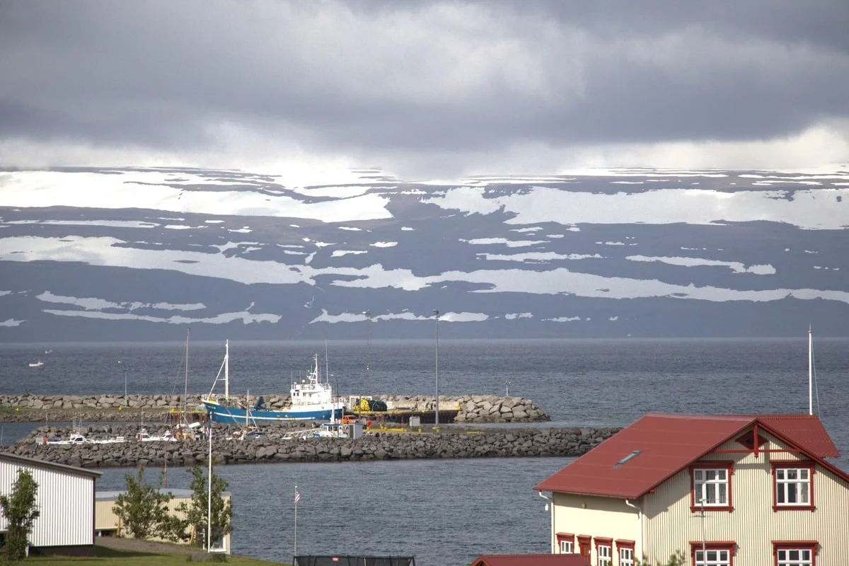 Petit port avec bateau de pêche bleu, montagnes enneigées en arrière-plan