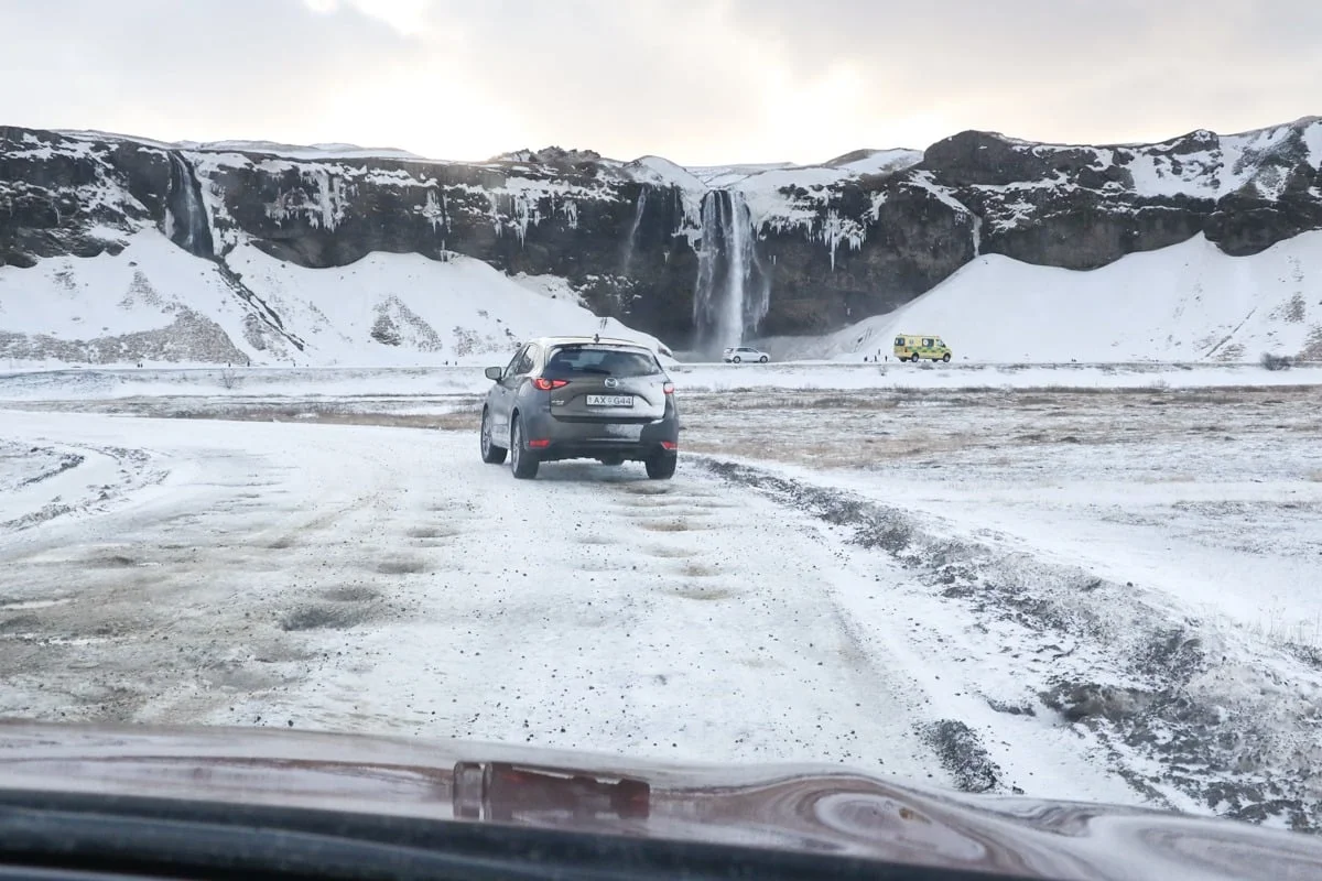 SUV de dos sur une piste enneigée face à une grande cascade