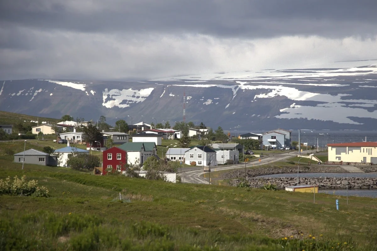 Petit village aux maisons colorées entouré de prairies vertes et montagnes enneigées