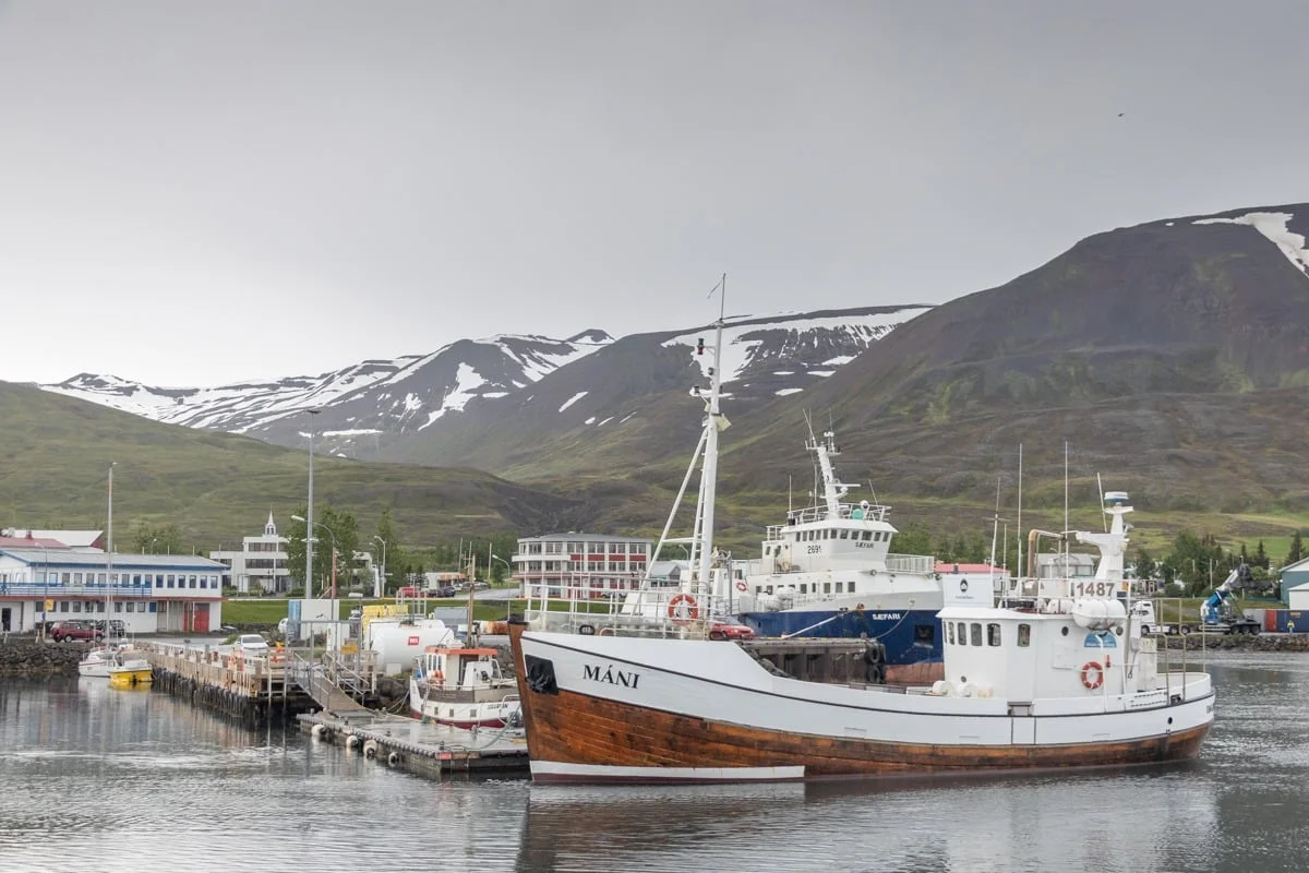 Bateau de pêche en bois amarré dans un port face à des montagnes enneigées