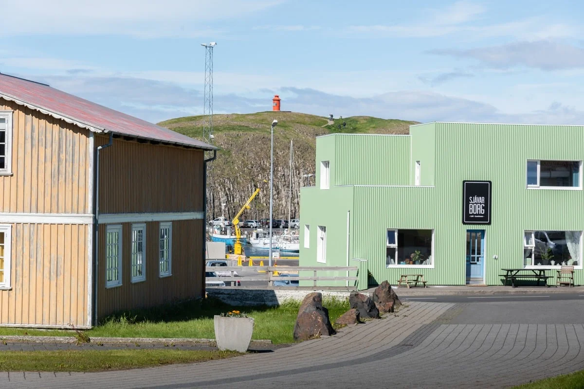 Bâtiments colorés autour d'un port avec un petit phare rouge sur une colline