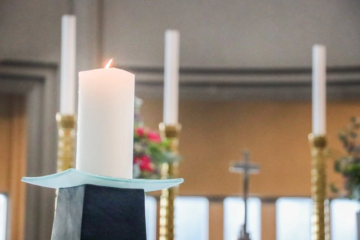 Grande bougie blanche allumée sur un autel avec chandelier doré en fond