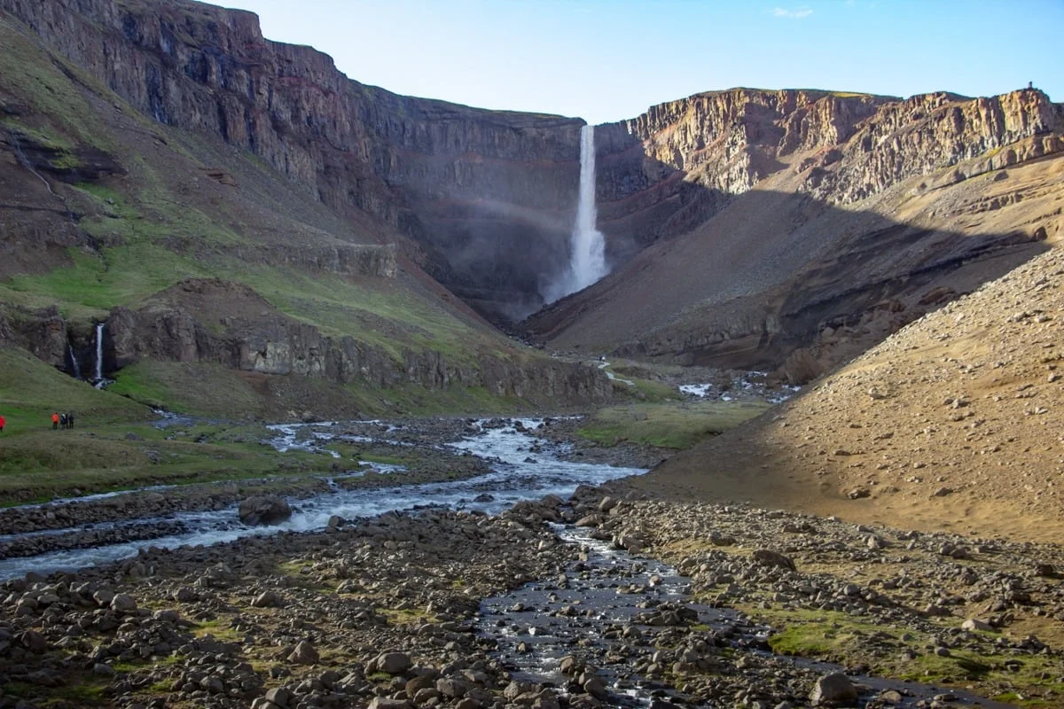 Grande cascade tombant dans un canyon volcanique avec rivière rocailleuse au premier plan