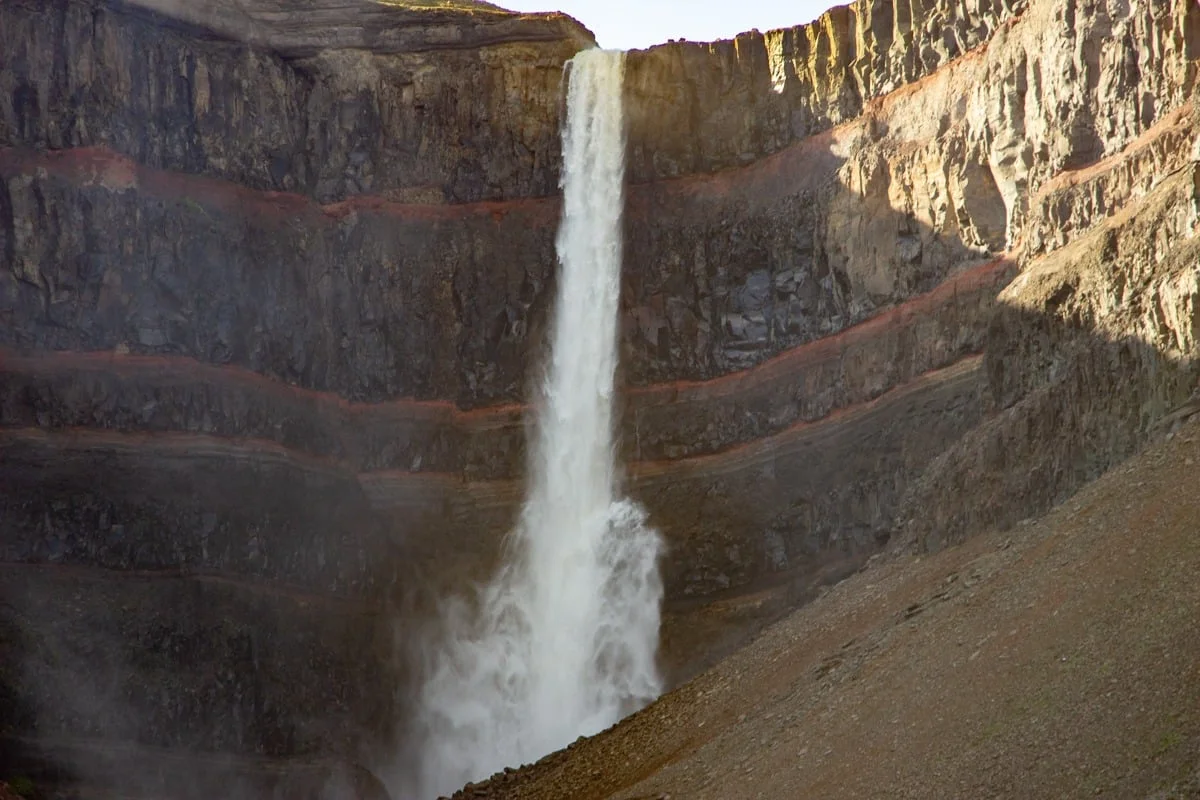 Haute cascade blanche tombant dans un amphithéâtre de falaises basaltiques stratifiées