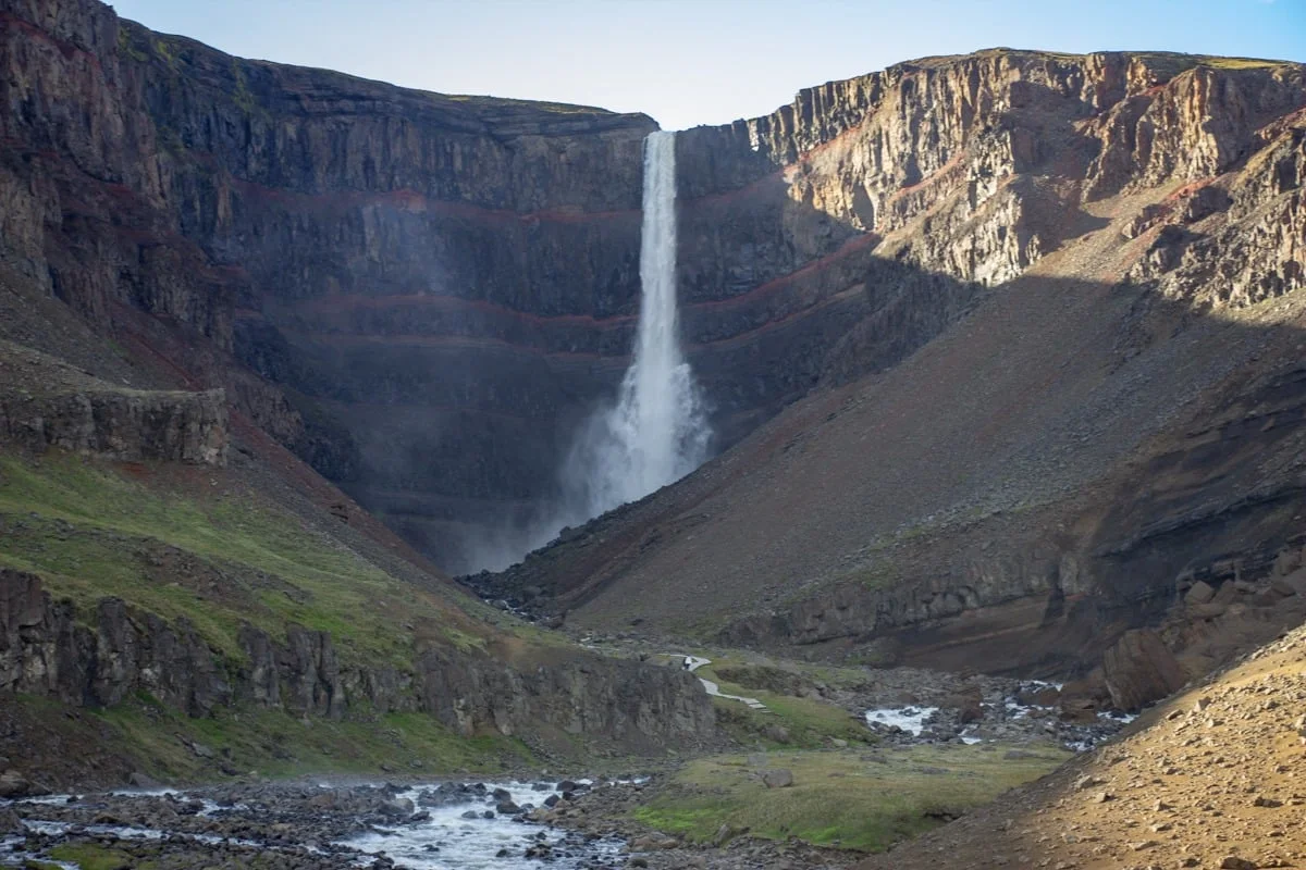 Grande cascade tombant d'une falaise basaltique striée de rouge dans une vallée rocheuse