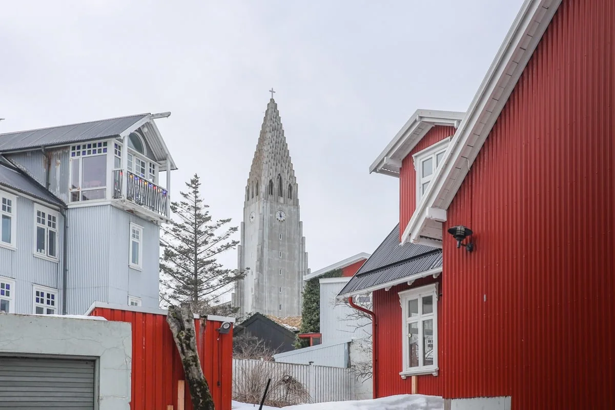 Clocher d'église en béton encadré par des maisons colorées en bois