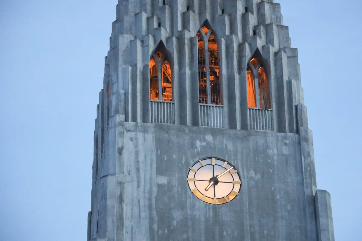 Tour d'église en béton avec horloge et fenêtres illuminées en orange
