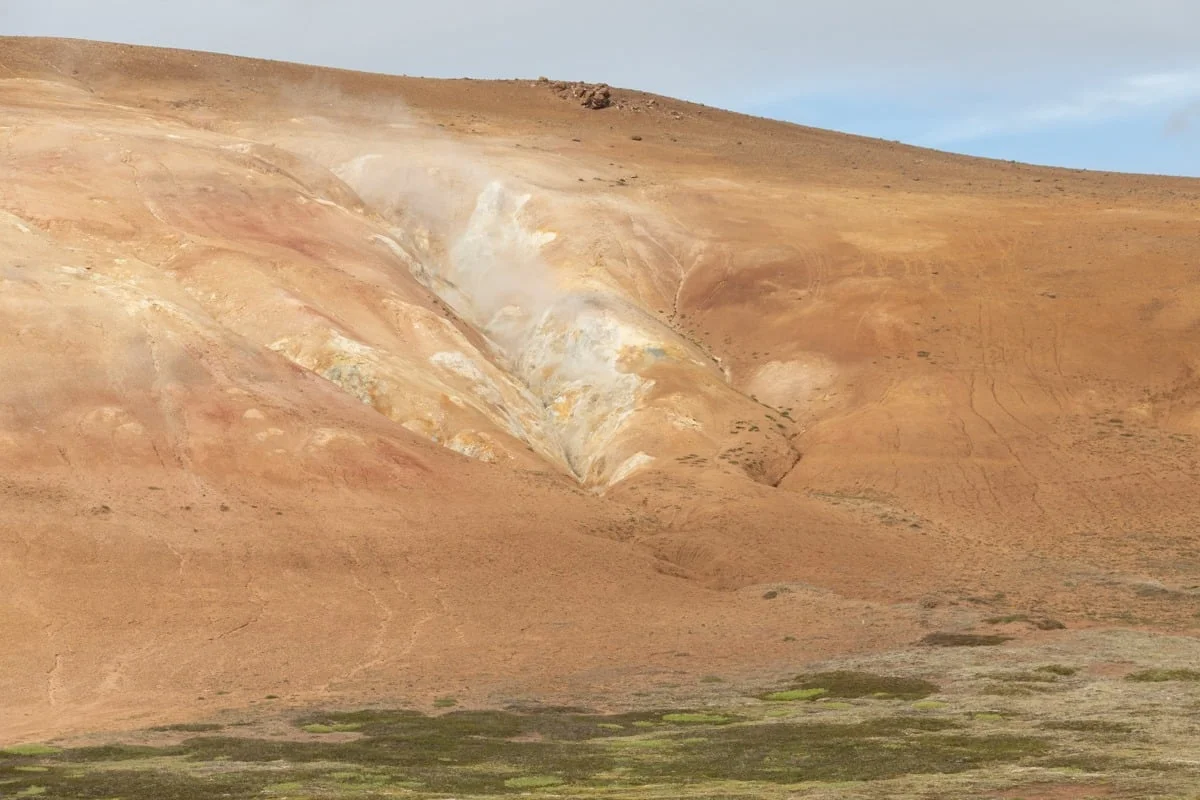 Colline volcanique ocre avec fumerolles et dépôts minéraux colorés