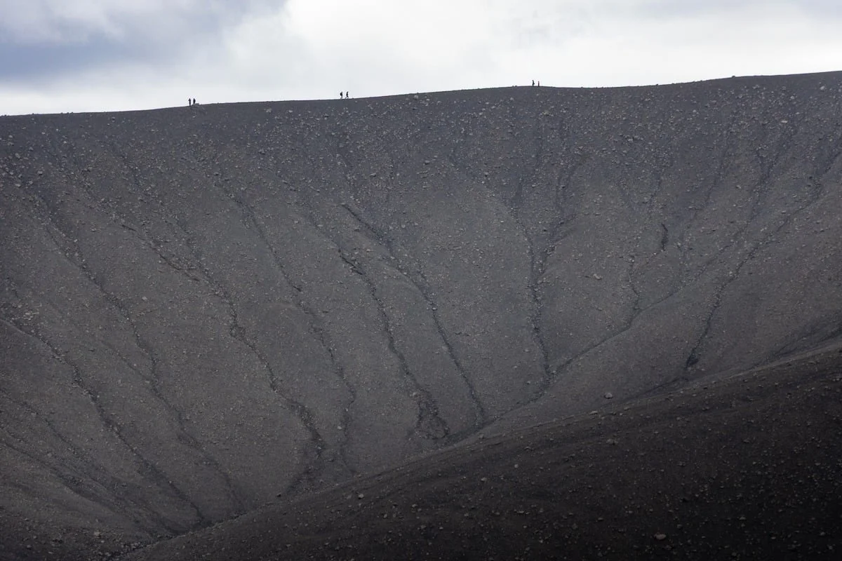 Flanc de cratère volcanique sombre avec randonneurs sur la crête