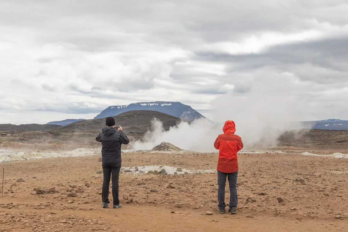 Deux personnes photographient des fumerolles dans un paysage volcanique aride