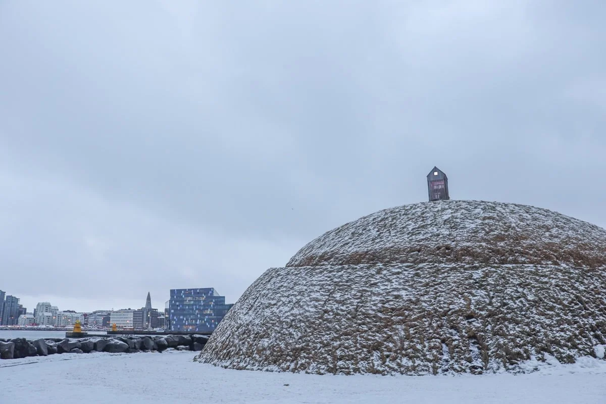 Grand dôme recouvert de gazon et neige avec petite cabane au sommet