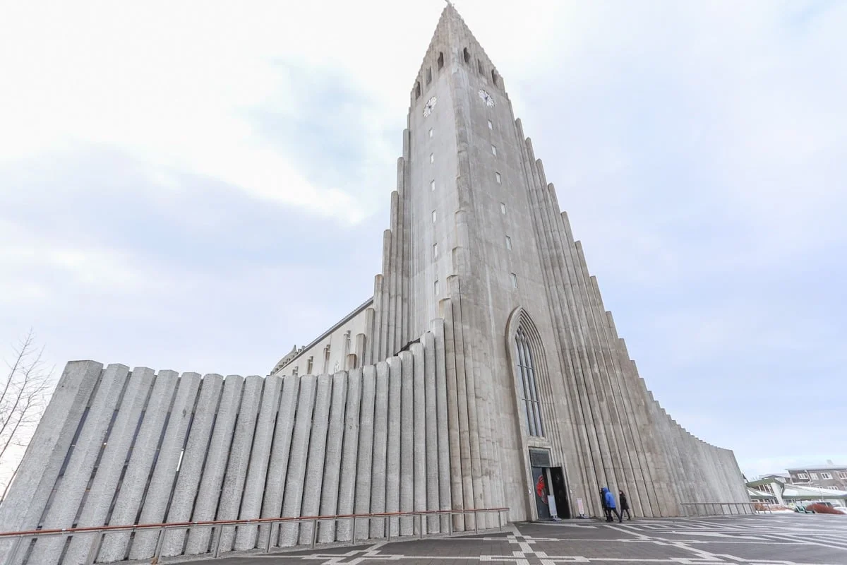 Église moderniste en béton avec clocher élancé sous ciel nuageux