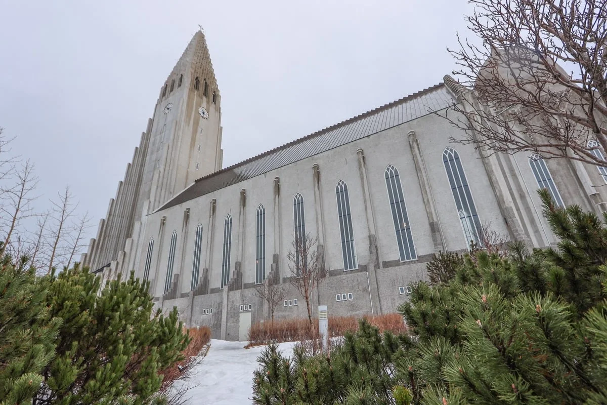 Grande église en béton gris avec clocher élancé sous ciel couvert hivernal