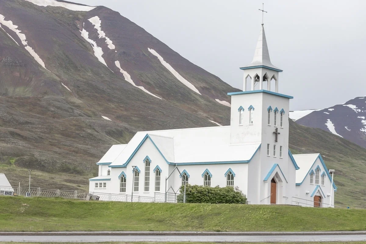 Église blanche aux détails bleus devant une montagne