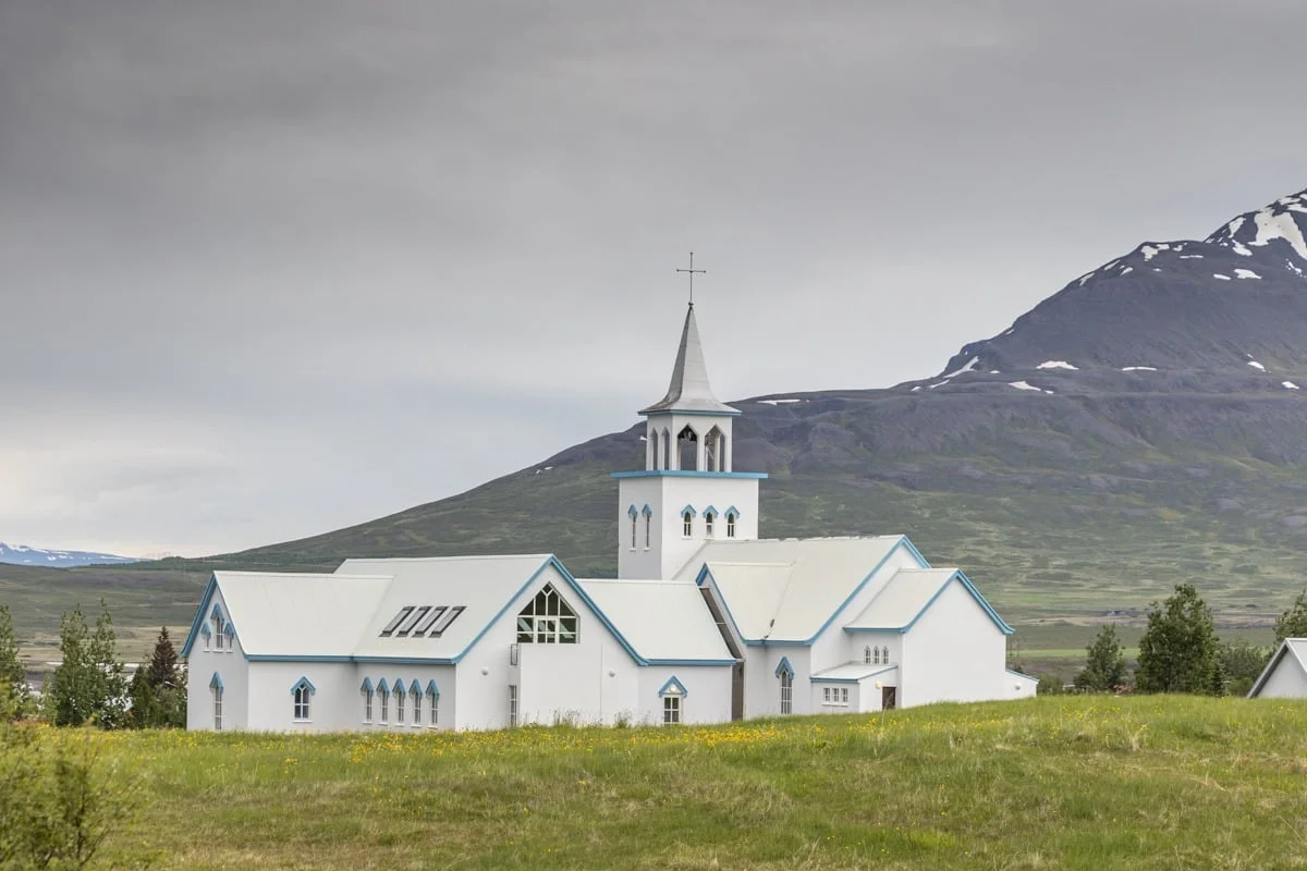 Église blanche aux bordures bleues entourée d'une prairie verdoyante et d'une montagne