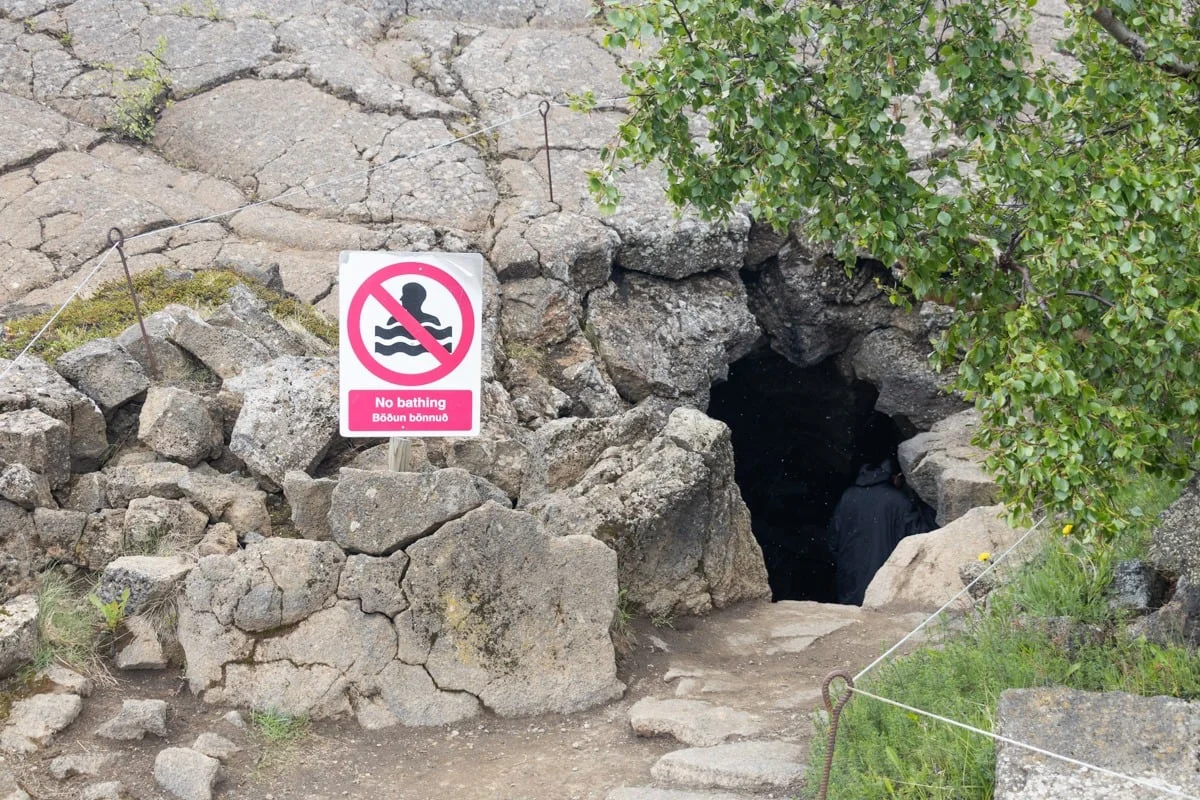 Entrée d'une grotte rocheuse avec panneau interdiction de se baigner
