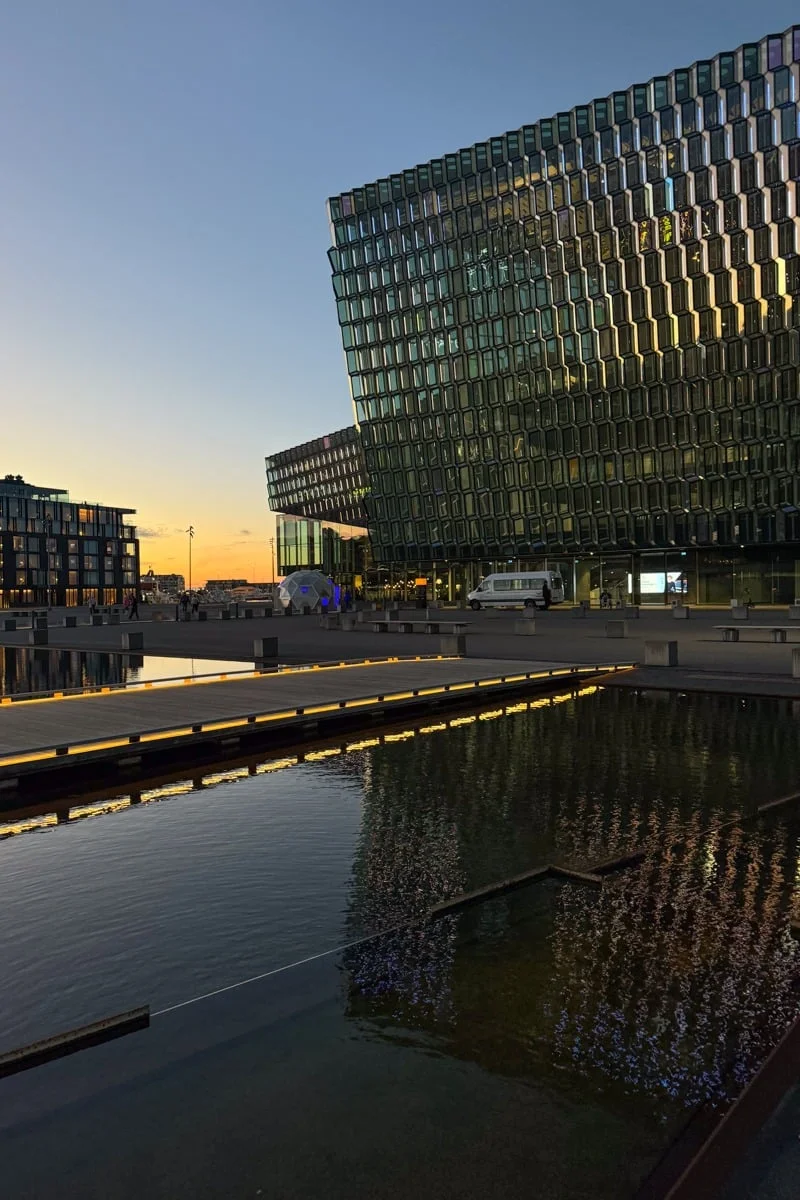 Façade en verre d'un bâtiment moderne reflétée dans un bassin au coucher du soleil