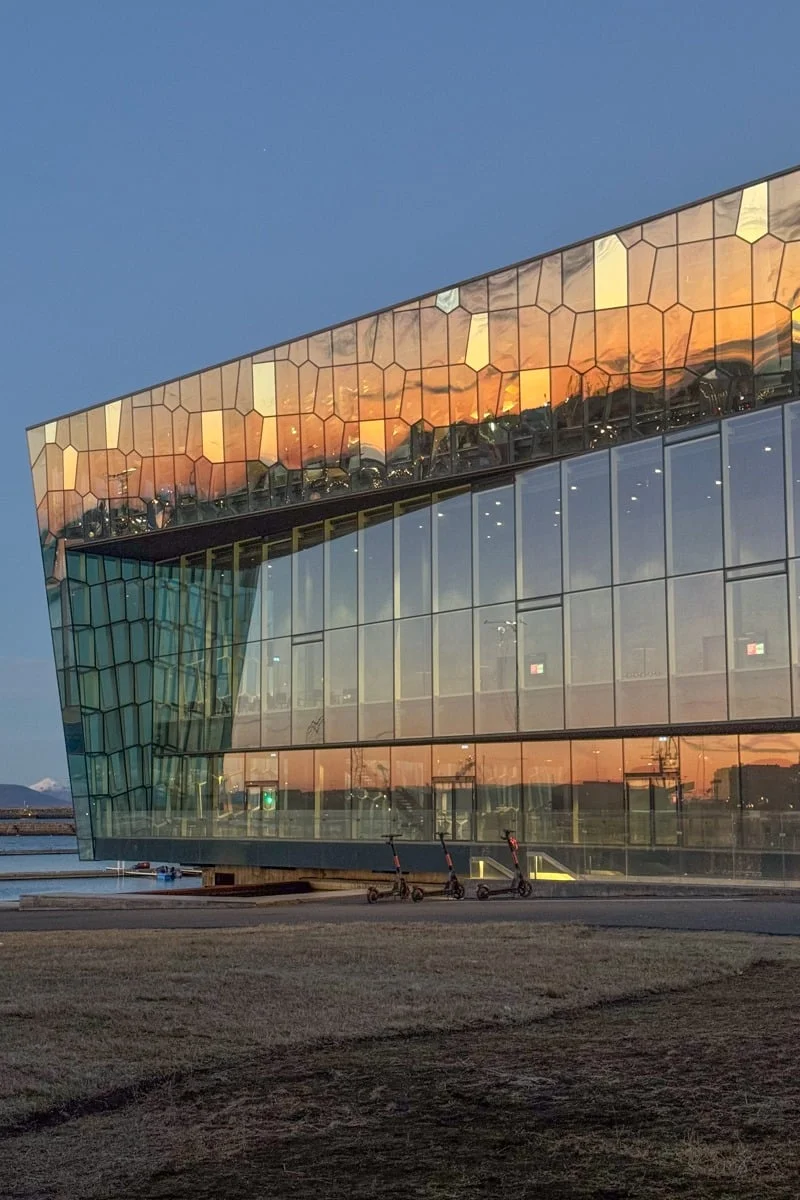 Façade en verre d'un bâtiment moderne reflétant un coucher de soleil doré