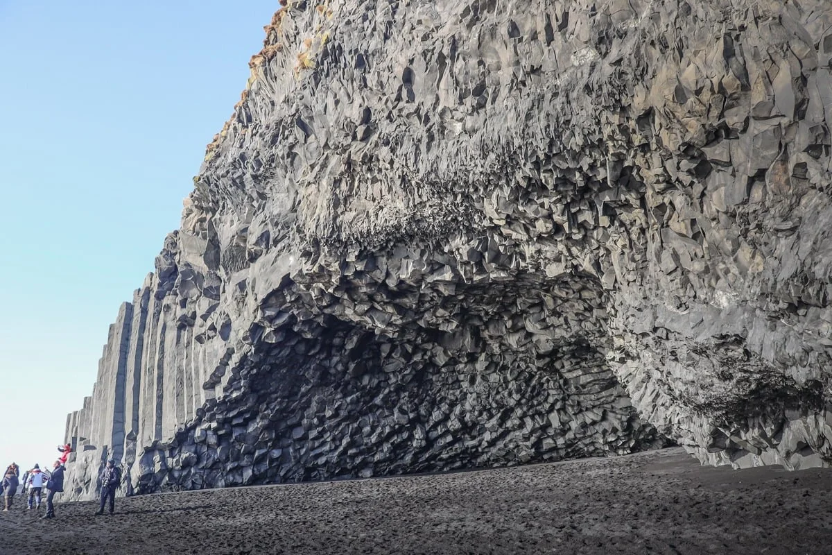 Falaise de colonnes basaltiques noires avec touristes au pied