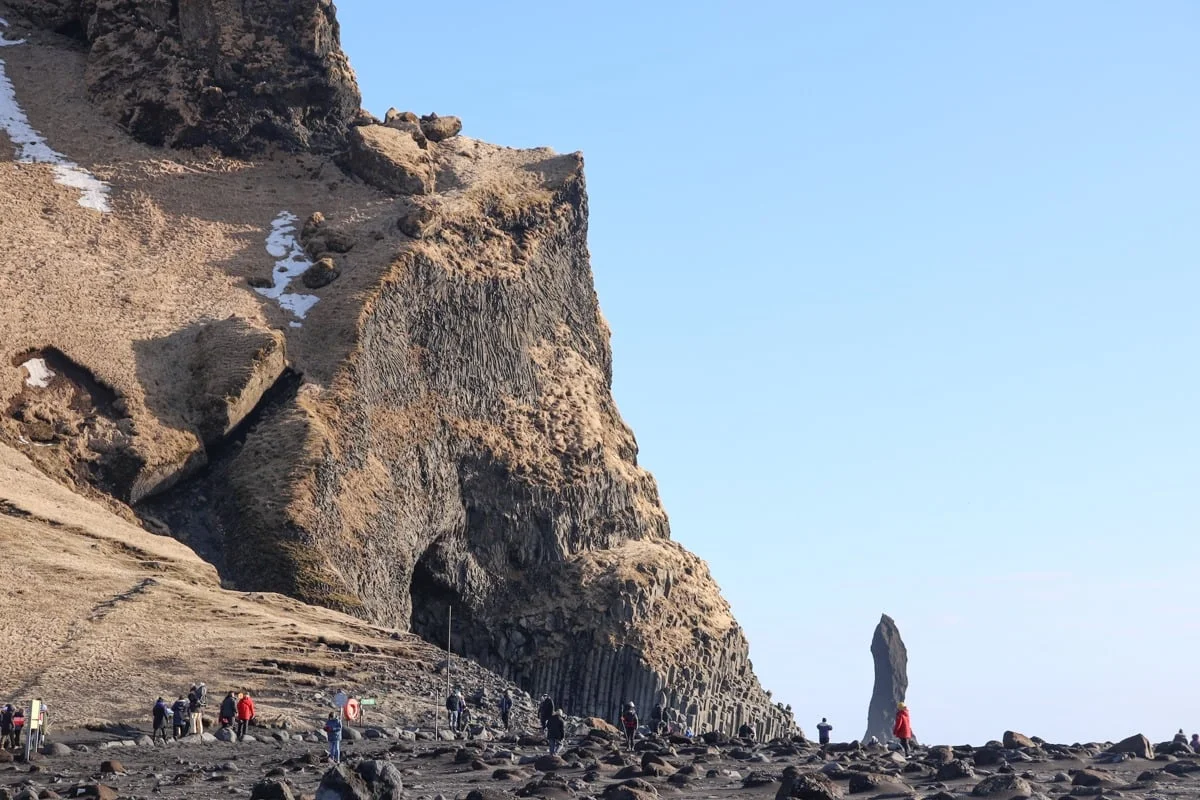 Falaise de basalte avec colonnes et rocher isolé, visiteurs sur plage noire