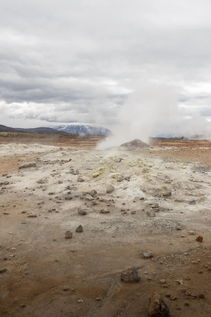 Fumerolle crachant de la vapeur sur un sol volcanique ocre et pierreux