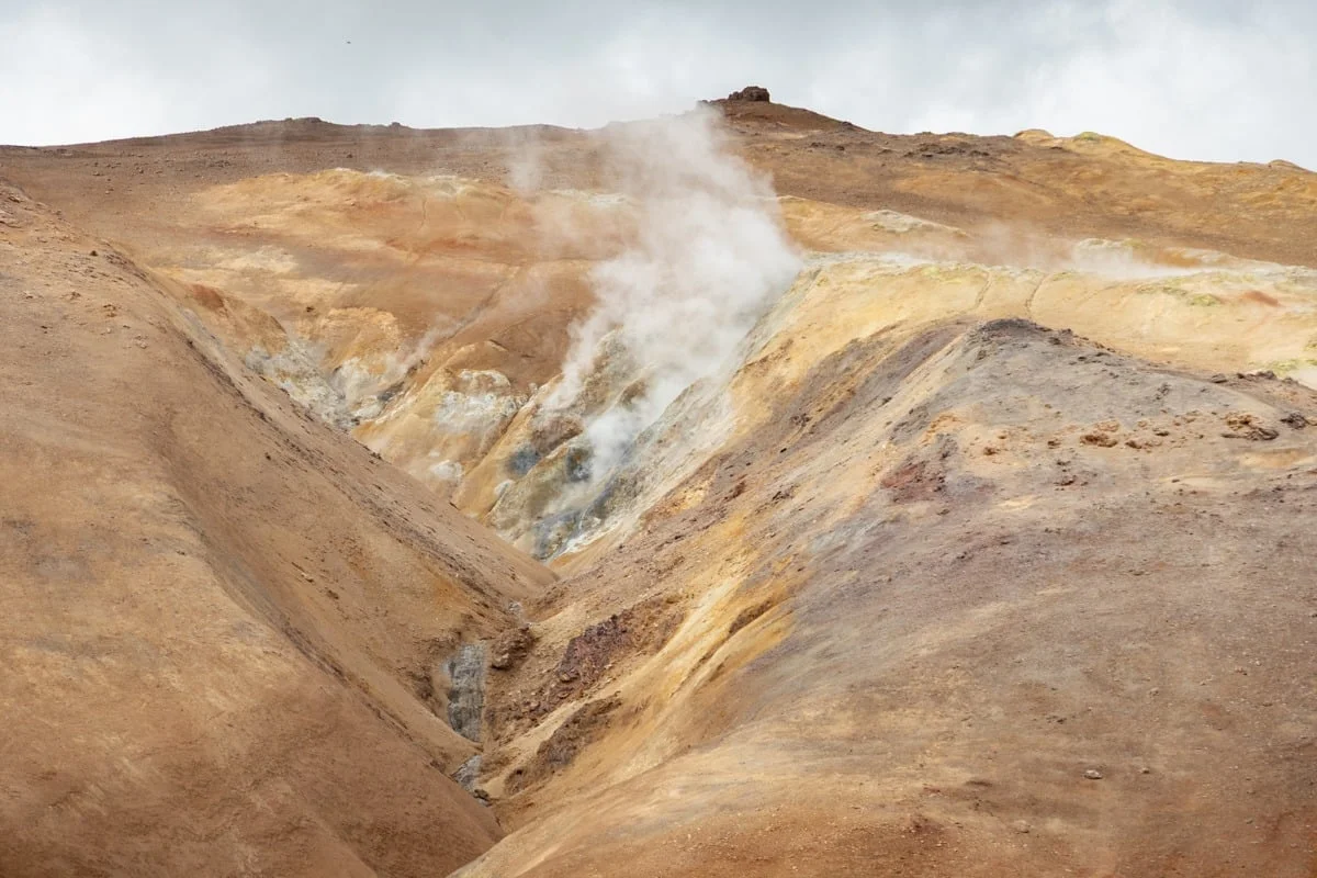 Collines volcaniques ocre avec fumerolles de vapeur blanche