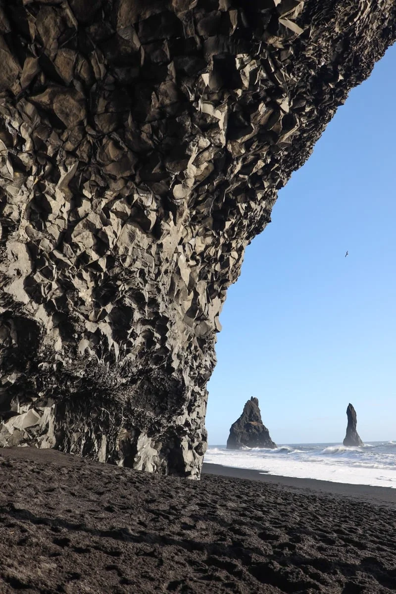 Falaise rocheuse basaltique ouvrant sur une plage de sable noir et des rochers