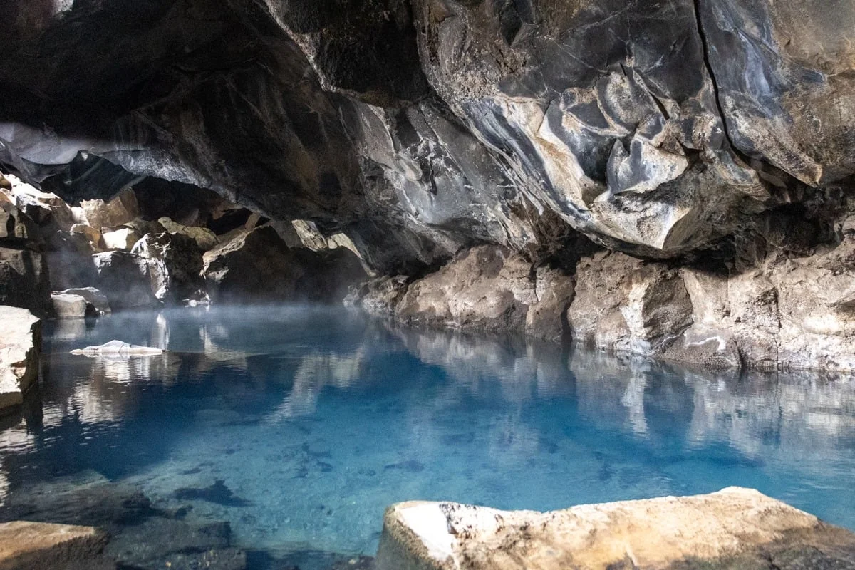 Piscine d'eau chaude bleue dans une grotte de lave avec vapeur