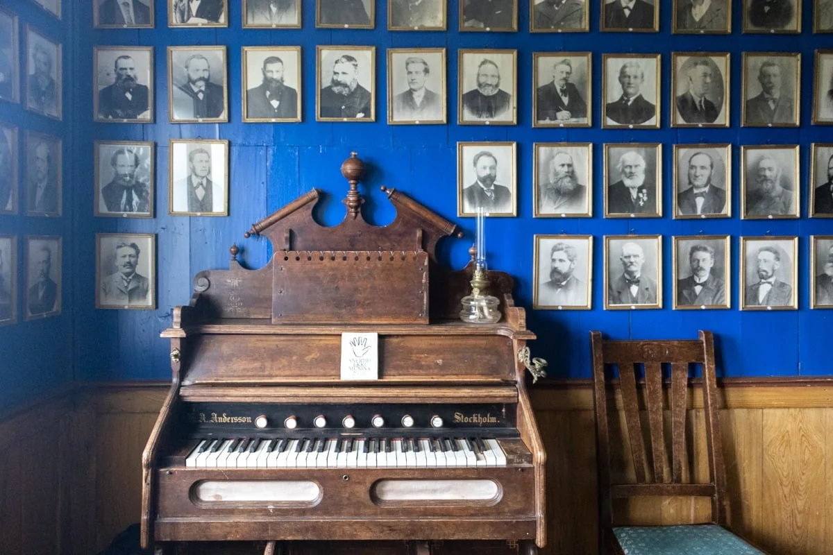 Vieil harmonium en bois devant un mur bleu orné de portraits anciens