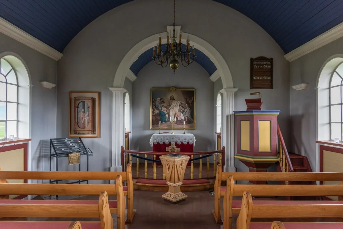 Intérieur d'une chapelle avec bancs en bois, autel et tableau religieux