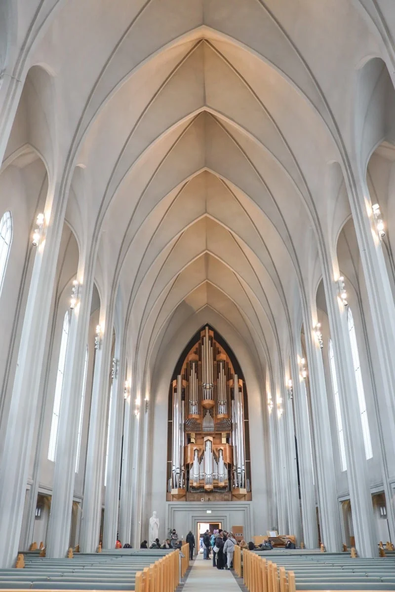 Nef cathédrale blanche avec grand orgue au fond et bancs en bois