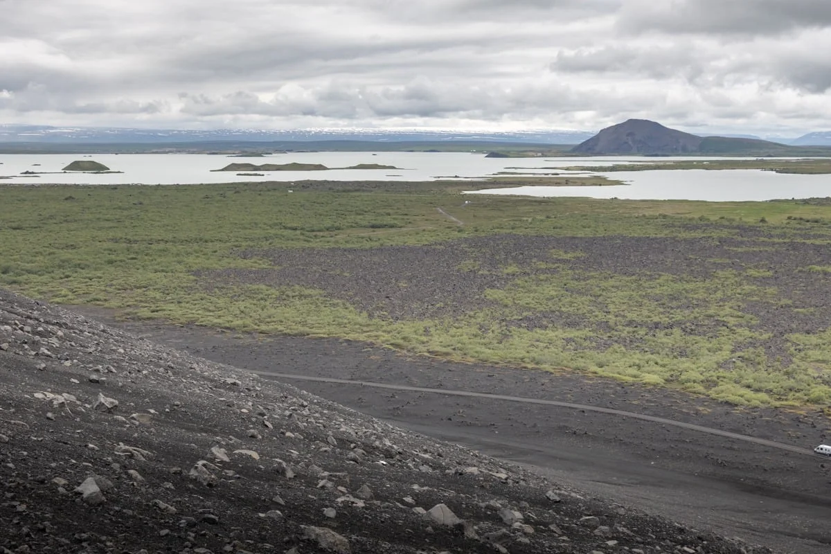 Paysage volcanique avec lac, végétation verte et cône volcanique au loin
