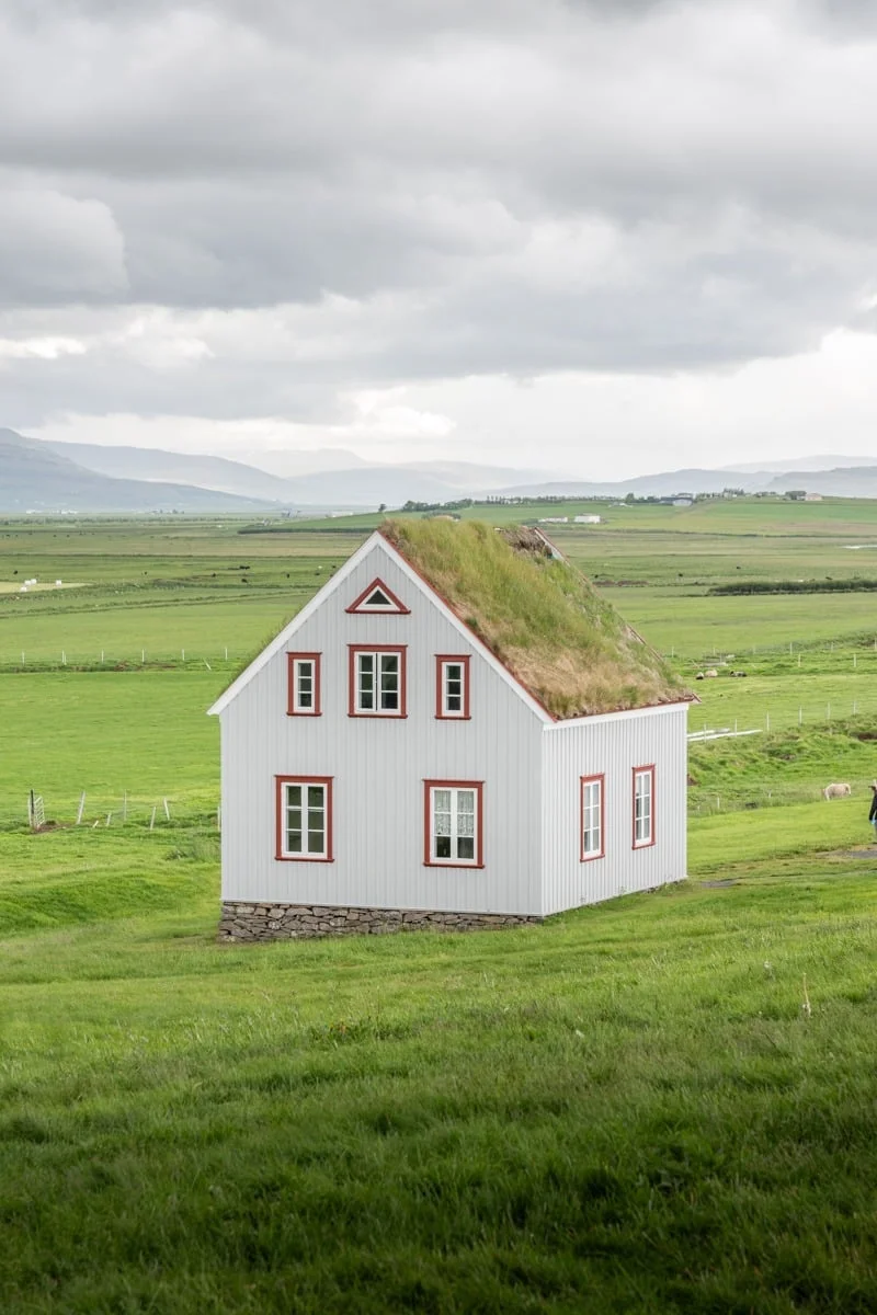 Petite maison blanche aux encadrements rouges avec toit en gazon dans une prairie verte