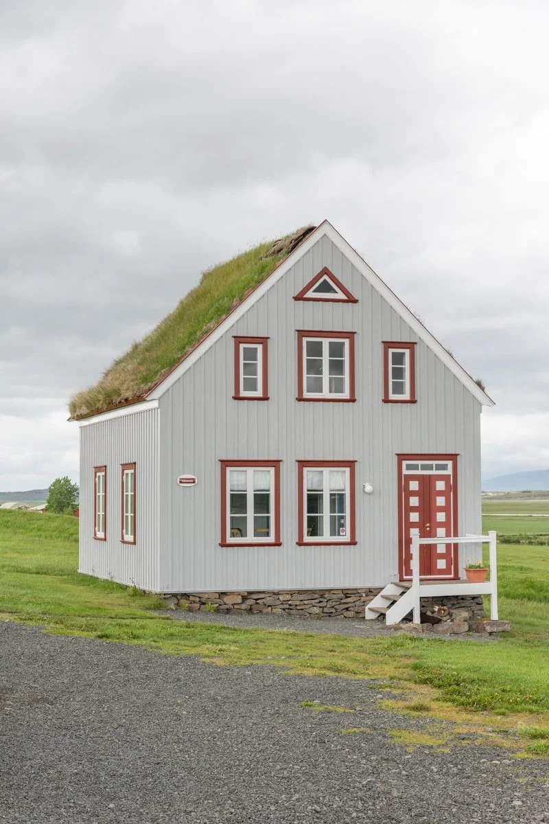 Maison en bois blanc avec toit végétalisé et encadrements rouges