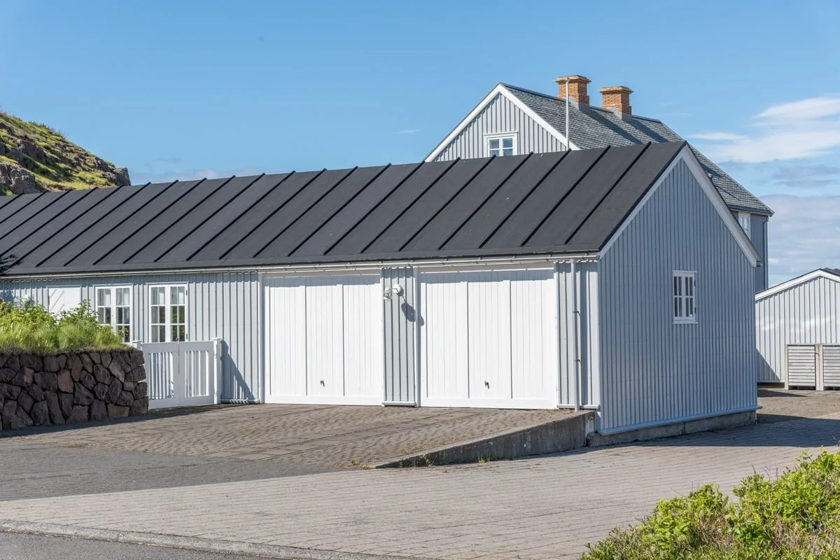Maison en bardage gris avec grand toit noir et portes de garage blanches