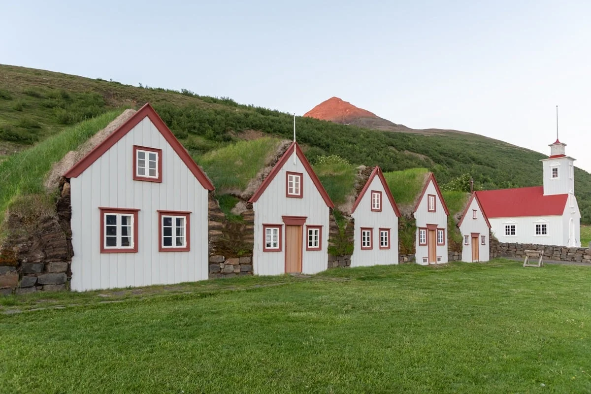 Rangée de maisons en tourbe blanches aux toits végétalisés et église blanche