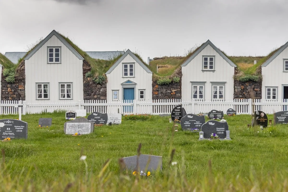 Maisons blanches aux toits de tourbe herbus devant un cimetière verdoyant