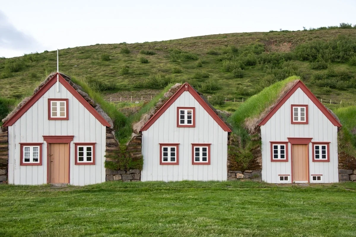 Trois maisons blanches aux toits de tourbe verte et encadrements rouges