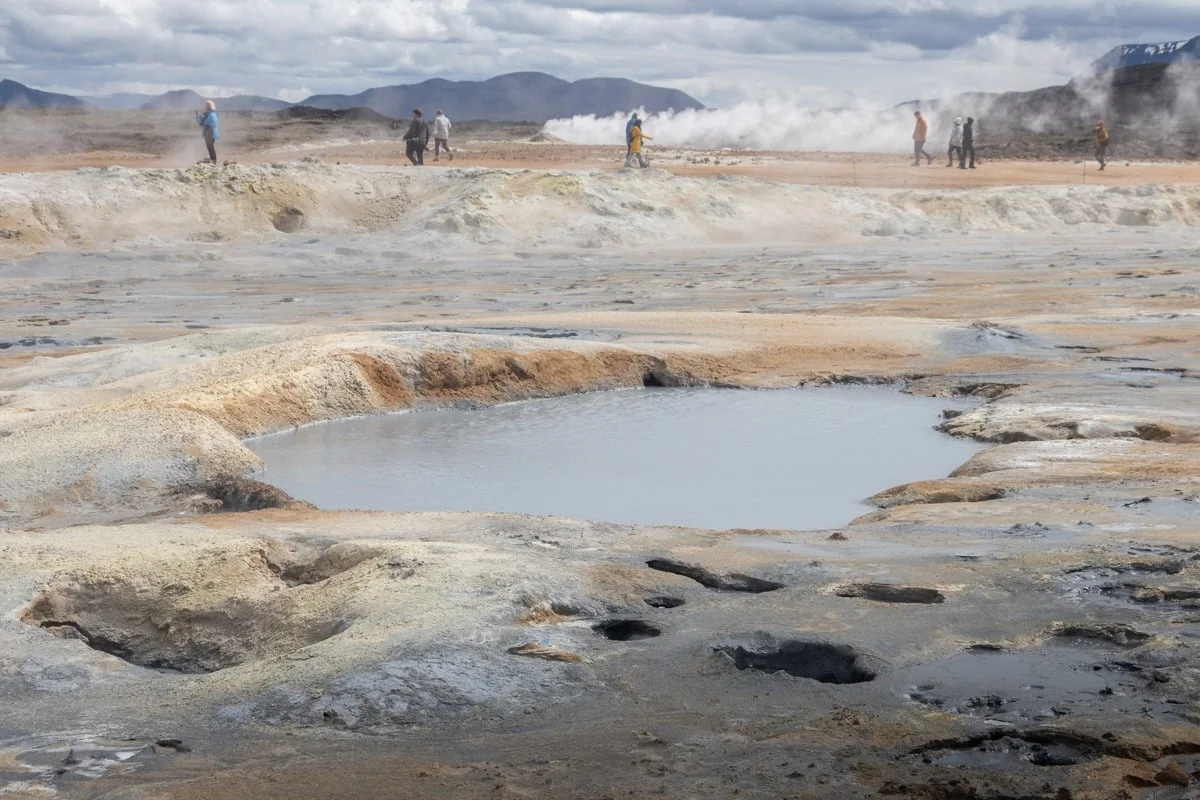 Mare de boue grise entourée de terrain volcanique avec visiteurs