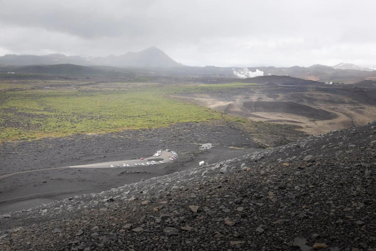 Vue plongeante sur un paysage volcanique noir avec parking et végétation verte