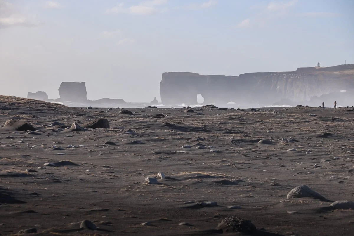 Plage de sable noir avec falaises et arche rocheuse