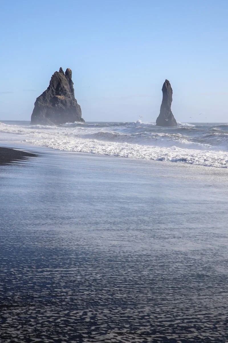 Deux rochers volcaniques émergent d'une mer agitée près d'une plage de sable noir