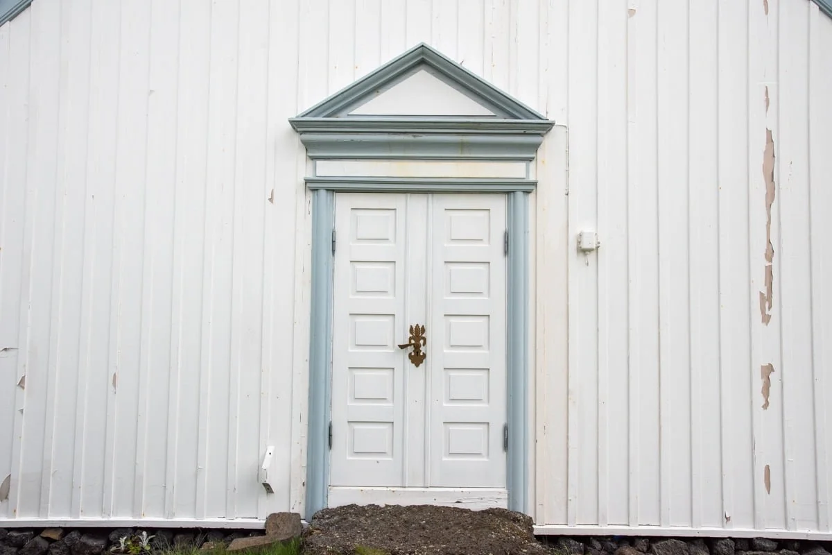 Porte double blanche encadrée de bleu sur façade en bardage blanc