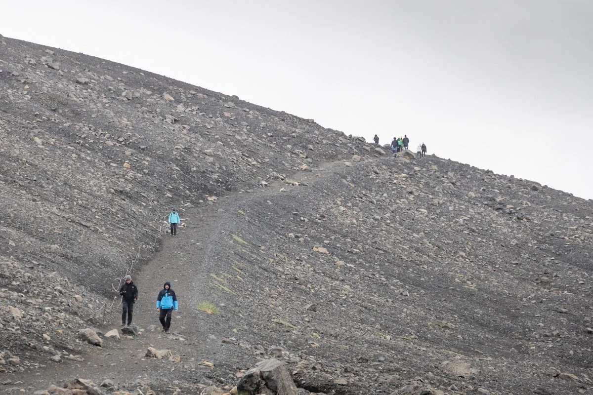 Groupe de randonneurs descendant un sentier sur pente volcanique rocheuse